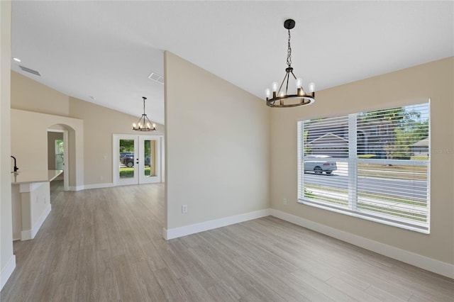 empty room featuring vaulted ceiling, arched walkways, french doors, and a notable chandelier