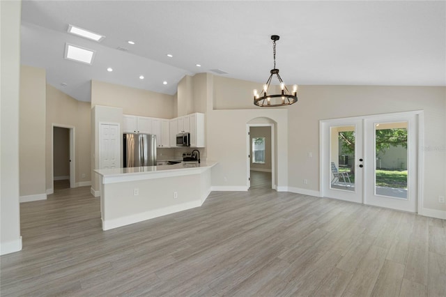 kitchen with light wood finished floors, light countertops, arched walkways, stainless steel appliances, and white cabinetry