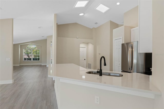 kitchen featuring freestanding refrigerator, light wood-type flooring, arched walkways, a sink, and vaulted ceiling