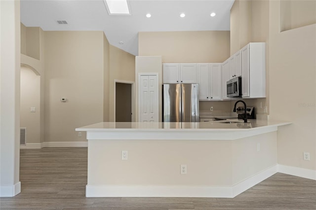 kitchen featuring baseboards, a peninsula, wood finished floors, and stainless steel appliances