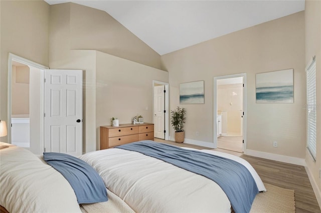 bedroom featuring baseboards, connected bathroom, wood finished floors, and high vaulted ceiling