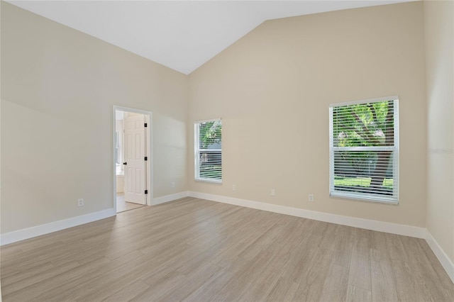 spare room with high vaulted ceiling, baseboards, and light wood-type flooring