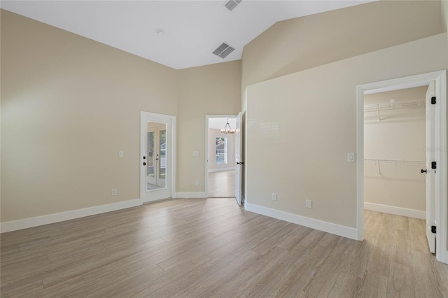 spare room featuring visible vents, baseboards, high vaulted ceiling, light wood finished floors, and a notable chandelier