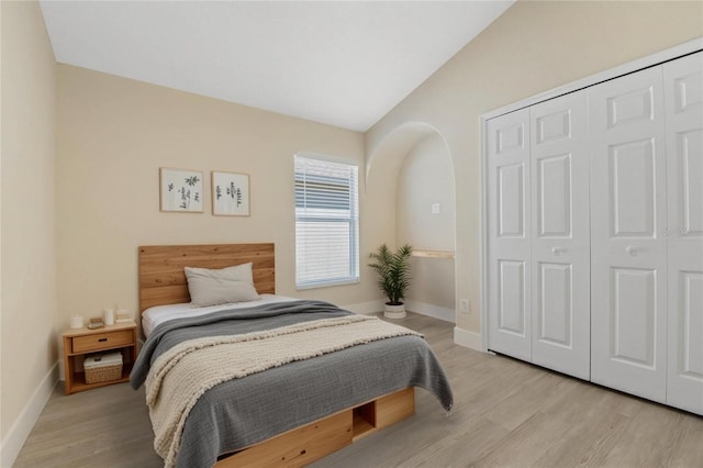 bedroom with vaulted ceiling, baseboards, a closet, and light wood finished floors