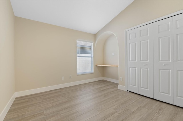 unfurnished bedroom with a closet, baseboards, lofted ceiling, and light wood-style floors