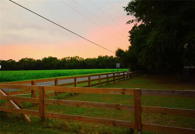 gate at dusk featuring fence, a yard, and a rural view