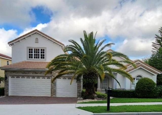 view of front facade with stucco siding, driveway, stone siding, an attached garage, and a tiled roof