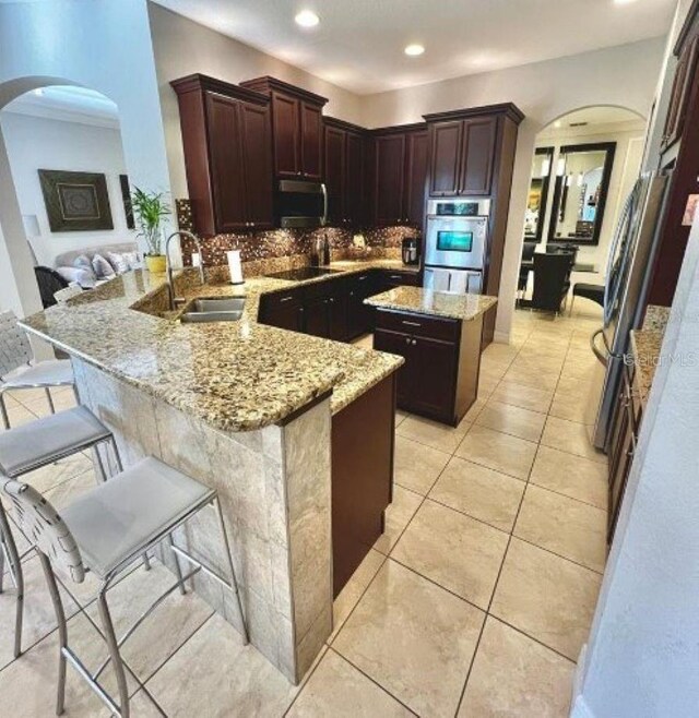 kitchen with stainless steel appliances, arched walkways, a peninsula, and a sink