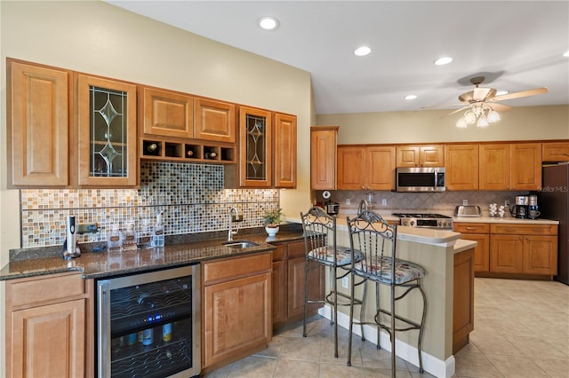 kitchen with a breakfast bar, beverage cooler, stove, ceiling fan, and stainless steel microwave