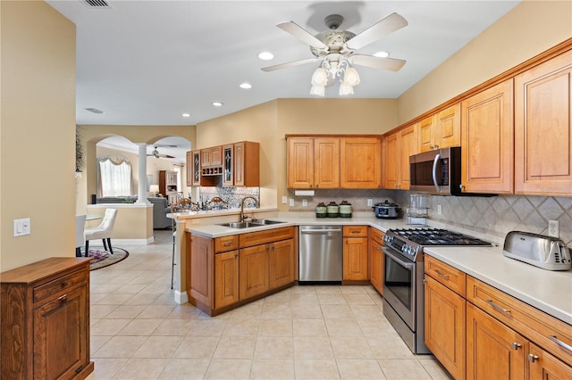 kitchen featuring ceiling fan, appliances with stainless steel finishes, a sink, arched walkways, and backsplash