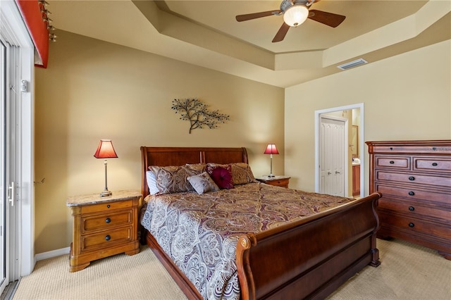 bedroom featuring light colored carpet, a raised ceiling, baseboards, ensuite bathroom, and visible vents