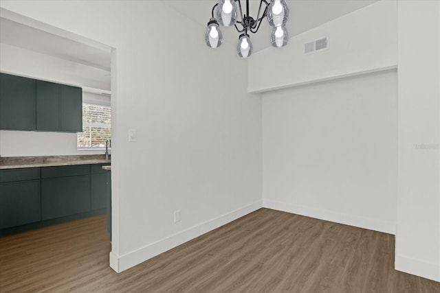 unfurnished dining area with an inviting chandelier, baseboards, wood finished floors, and visible vents