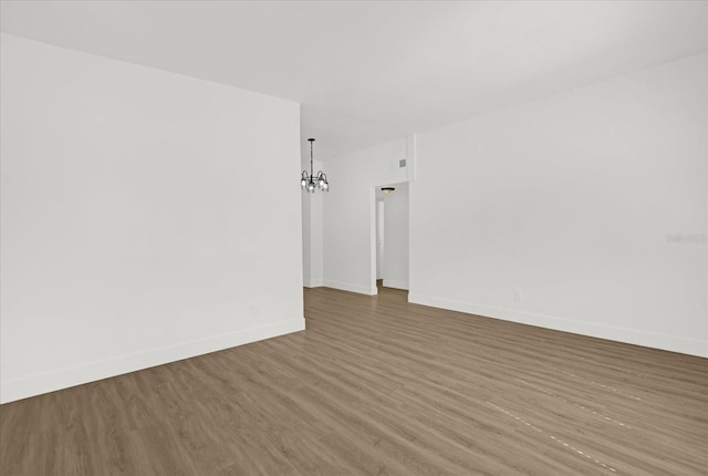unfurnished room featuring baseboards, wood finished floors, and a notable chandelier