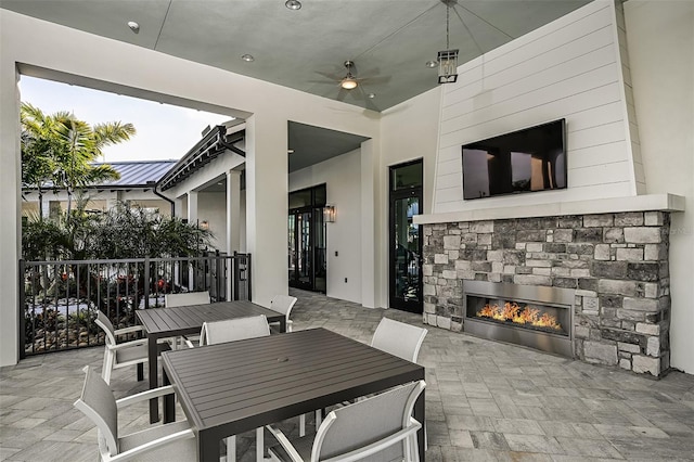 view of patio featuring outdoor dining area, a ceiling fan, and an outdoor stone fireplace