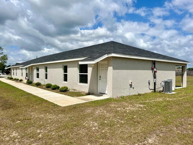 view of side of property featuring stucco siding, central AC, and a yard