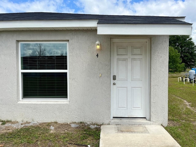 property entrance featuring a shingled roof and stucco siding
