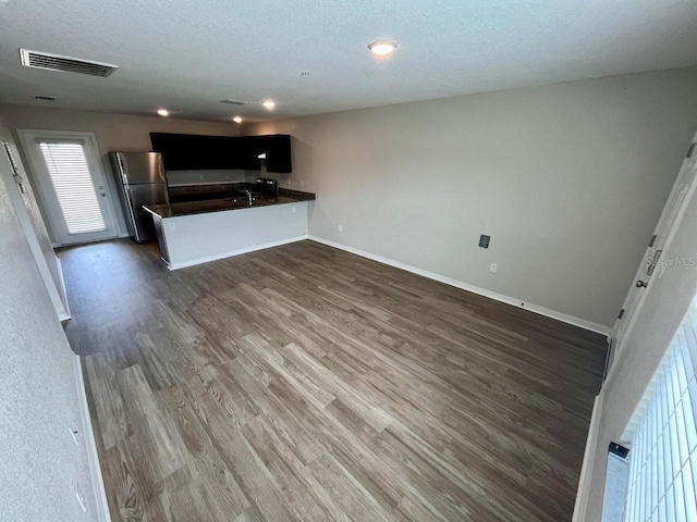 kitchen with visible vents, dark countertops, freestanding refrigerator, a peninsula, and dark wood-type flooring