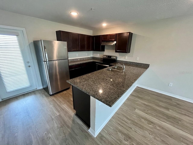 kitchen featuring a sink, dark stone countertops, stainless steel appliances, a peninsula, and under cabinet range hood