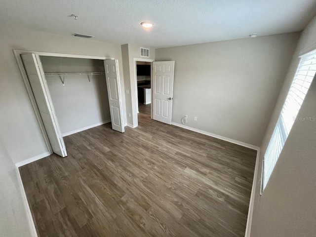 unfurnished bedroom with dark wood-style flooring, baseboards, visible vents, and a closet