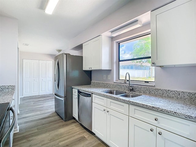kitchen featuring light stone counters, a sink, white cabinetry, light wood-style floors, and stainless steel appliances