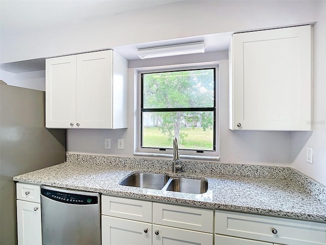 kitchen featuring light stone countertops, a sink, stainless steel dishwasher, and white cabinets