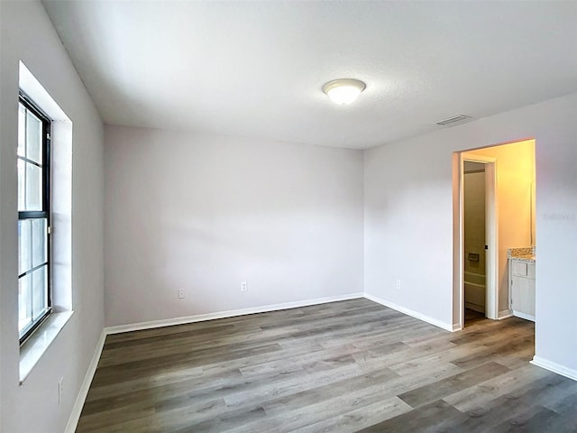 unfurnished bedroom featuring wood finished floors, visible vents, and multiple windows