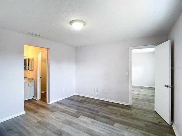 unfurnished bedroom with a textured ceiling, visible vents, wood finished floors, and baseboards