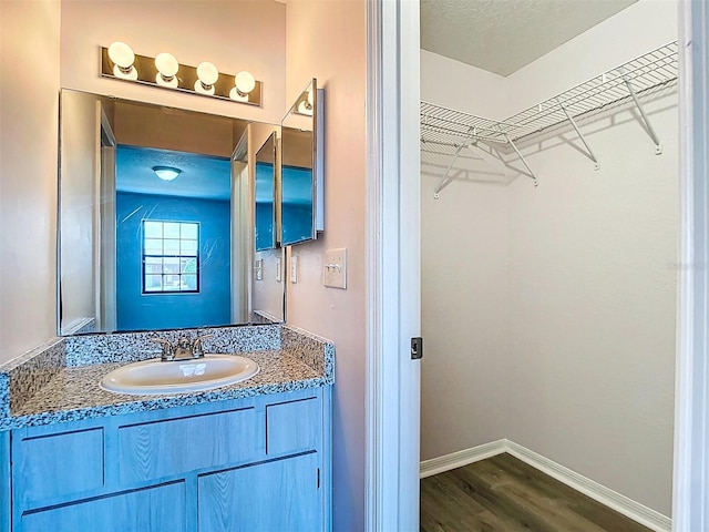 bathroom featuring vanity, a walk in closet, baseboards, and wood finished floors