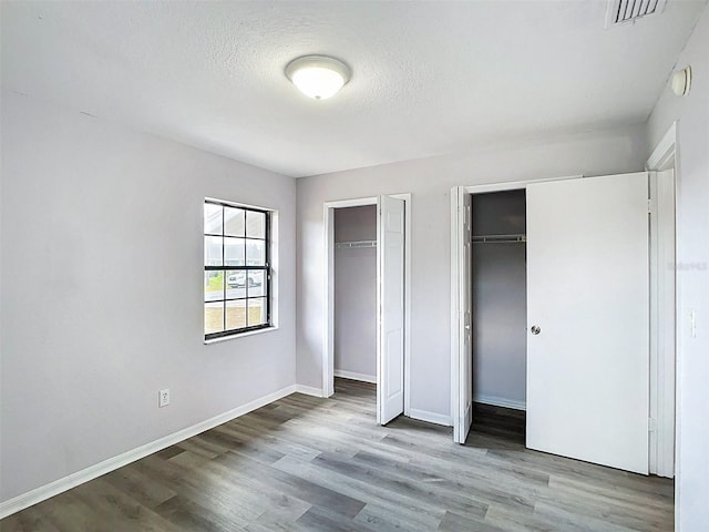 unfurnished bedroom with wood finished floors, a textured ceiling, visible vents, two closets, and baseboards