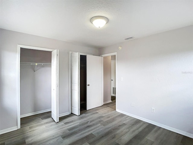 unfurnished bedroom featuring two closets, baseboards, visible vents, and wood finished floors