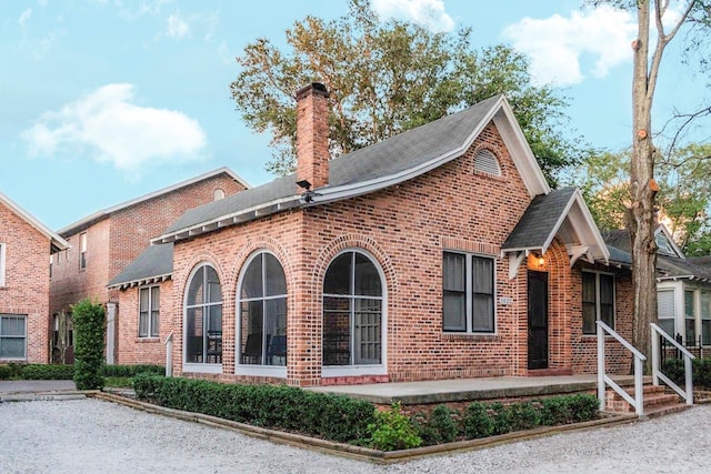 view of front facade featuring brick siding, a chimney, and a shingled roof