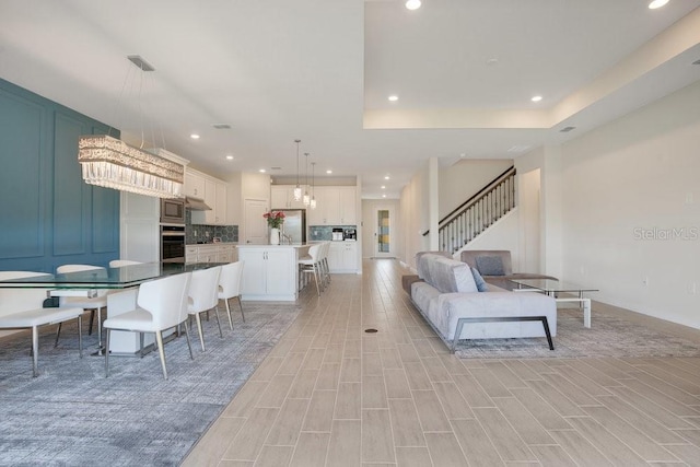 living area with recessed lighting, stairs, light wood-type flooring, a raised ceiling, and baseboards