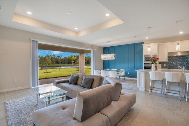 living room featuring light wood-style flooring, a water view, a raised ceiling, recessed lighting, and baseboards