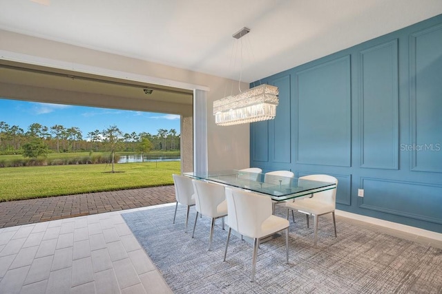 dining area with a water view, a decorative wall, and a chandelier