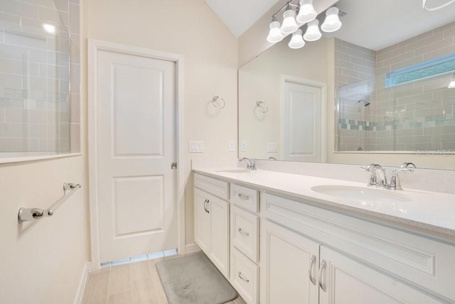 bathroom featuring tiled shower, double vanity, baseboards, and vaulted ceiling