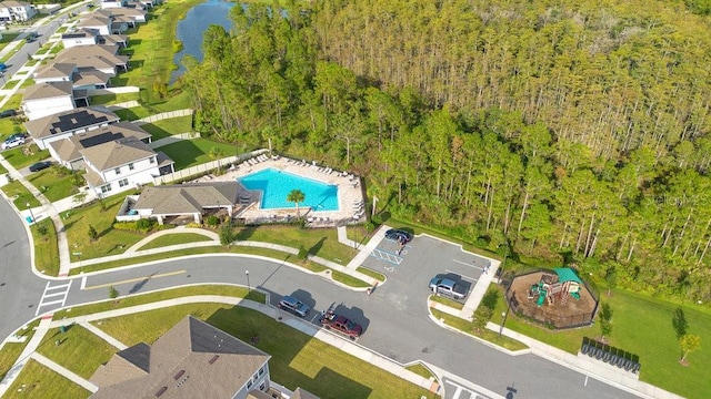 aerial view of property and surrounding area featuring a pool, a nearby body of water, and a forest