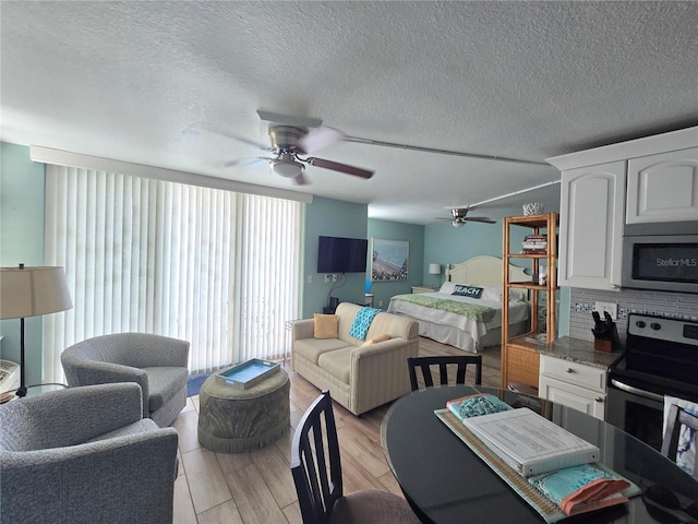 living room with a ceiling fan, a textured ceiling, and light wood-style floors