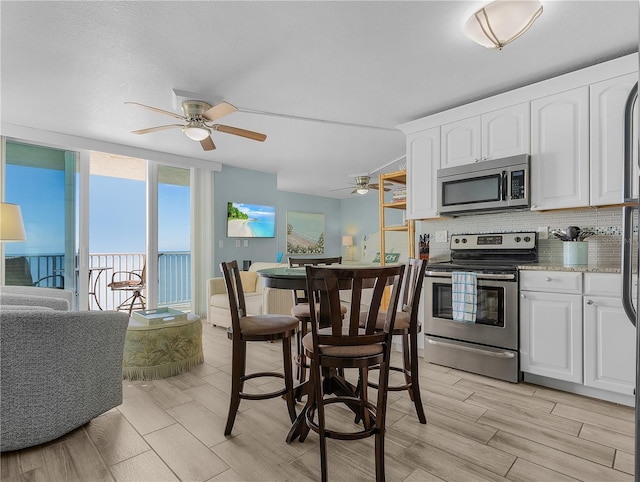 kitchen with stainless steel appliances, a ceiling fan, wood tiled floors, decorative backsplash, and white cabinets