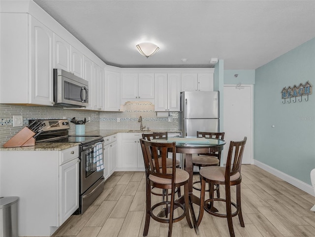 kitchen with stainless steel appliances, light wood-type flooring, a sink, white cabinetry, and decorative backsplash
