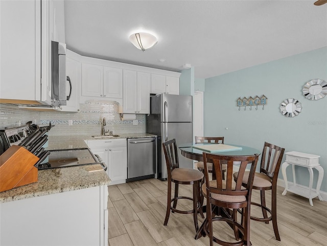 kitchen with stainless steel appliances, a sink, decorative backsplash, and light wood-style flooring