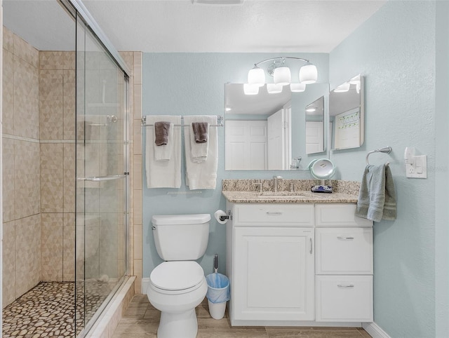 bathroom with a stall shower, toilet, vanity, baseboards, and a textured wall