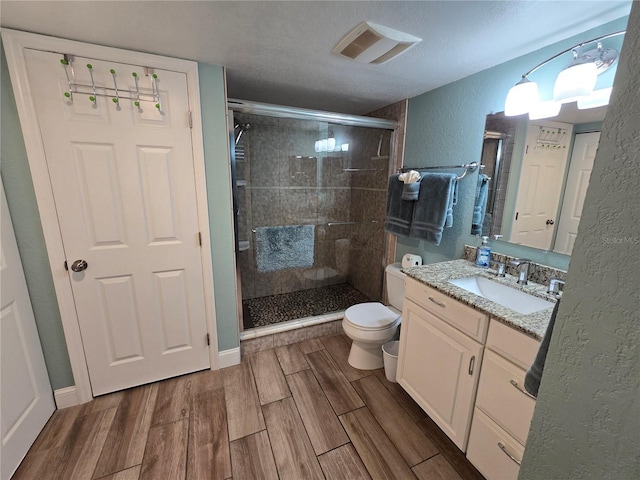 bathroom featuring a textured wall, a stall shower, wood finished floors, toilet, and vanity