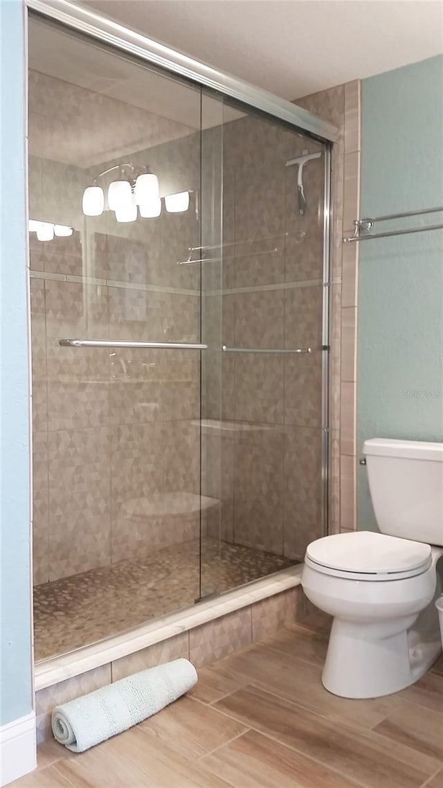full bath with toilet, a shower stall, and wood finished floors
