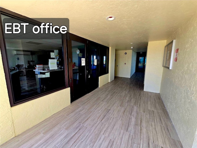 hallway featuring a textured wall, wood finished floors, and a textured ceiling