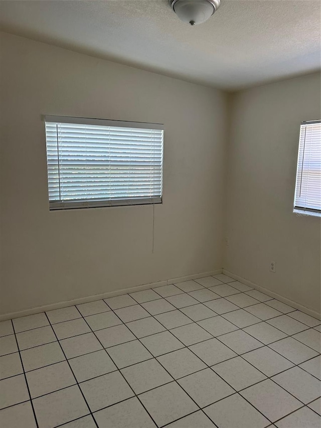 unfurnished room with light tile patterned flooring, a textured ceiling, and baseboards