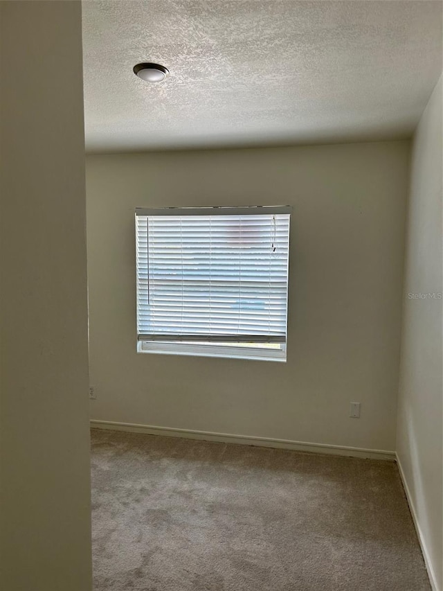 unfurnished room featuring a textured ceiling, carpet, and baseboards