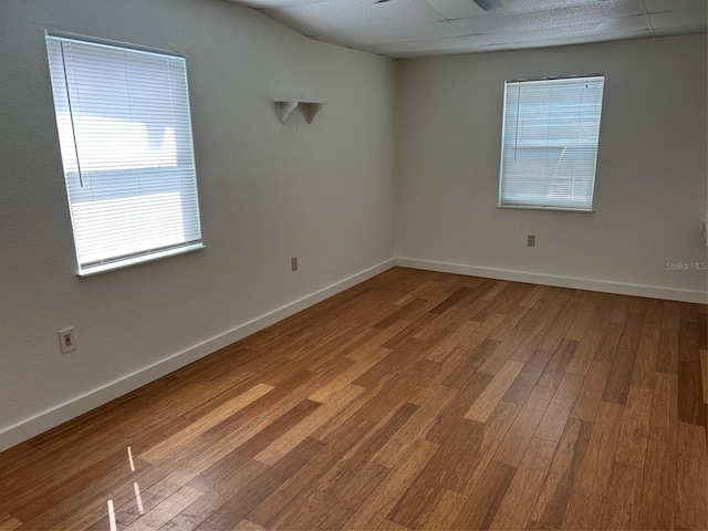 spare room with healthy amount of natural light, wood finished floors, and baseboards