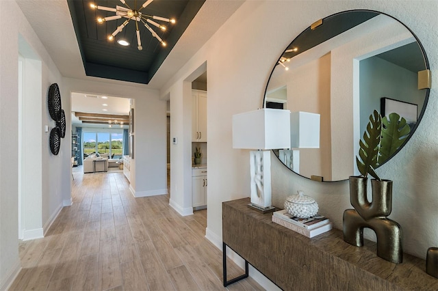1688 Lugano Cir, North Venice, FL 34275 - corridor with light wood-style flooring, a tray ceiling, a chandelier, and baseboards