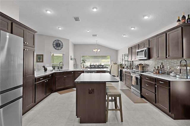 924 Figwood Loop, The Villages, FL 32163 - kitchen with stainless steel appliances, lofted ceiling, dark brown cabinetry, a peninsula, and a chandelier