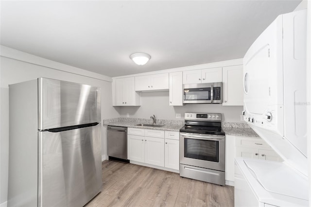 302 NW 7th Ter, Gainesville, FL 32601 - kitchen featuring stainless steel appliances, estacked washer and dryer, light wood-style floors, white cabinetry, and light stone countertops